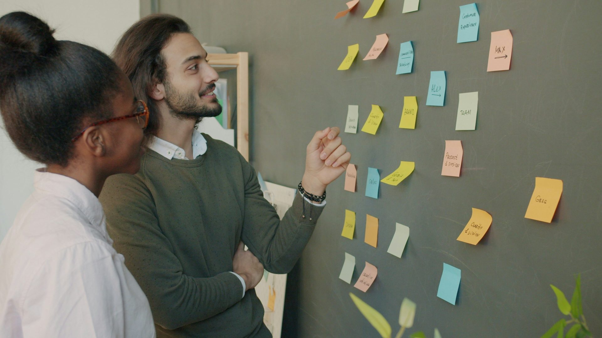 Two colleagues discuss sticky notes on a wall.